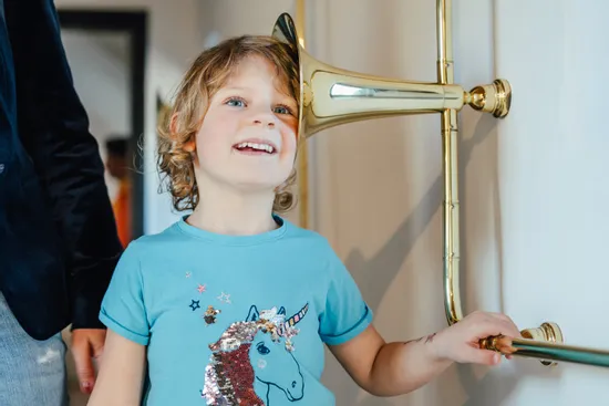 Lächelndes Kind mit Einhorn-Shirt hört durch antikes Messing-Sprachrohr
